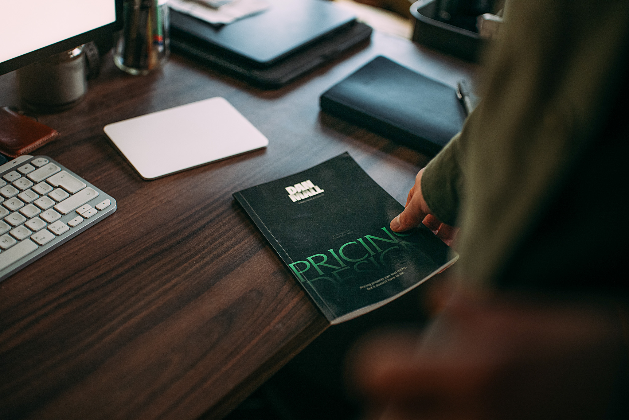 A person picking up a Pricing Design book from a desk